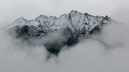 A breathtaking view of snow-covered mountain peaks surrounded by dense fog, creating a mystical landscape.