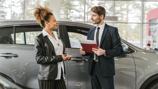 A woman discussing car purchase with a dealer inside a car dealership showroom.