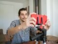Confident young man adjusting smartphone on tripod for home vlogging setup.