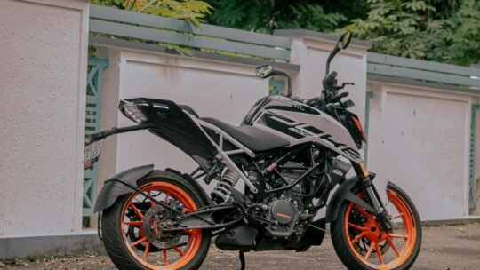 A stylish black and orange motorcycle parked near a white wall in an outdoor setting.
