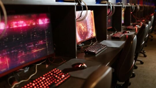 Row of gaming stations with illuminated keyboards and monitors in an esports arena.