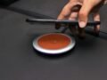Close-up of a hand placing a smartphone on a wireless charging pad on a leather surface.