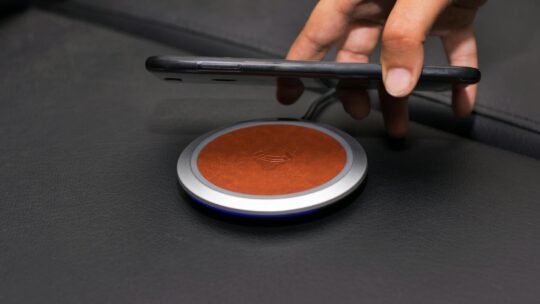 Close-up of a hand placing a smartphone on a wireless charging pad on a leather surface.