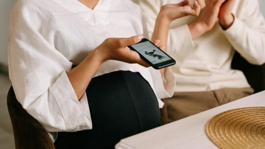 Pregnant woman holding smartphone indoors, capturing intimate family moments with technology.