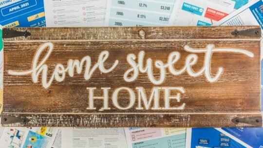 Rustic wooden 'Home Sweet Home' sign atop financial and real estate documents.