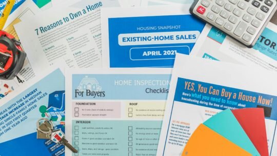 Flat lay of real estate brochures, checklists, and a calculator for home buying.