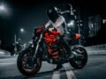 A biker on a red Ducati motorcycle rides through an illuminated city street at night.