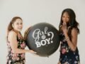 Two women holding a 'Girl or Boy?' balloon, celebrating a gender reveal.