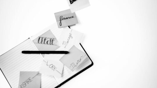 Black and white image featuring a workspace with inspiring handwritten notes and a notebook.