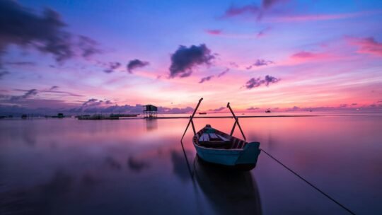 A tranquil tropical sunrise with a lone boat on calm waters.
